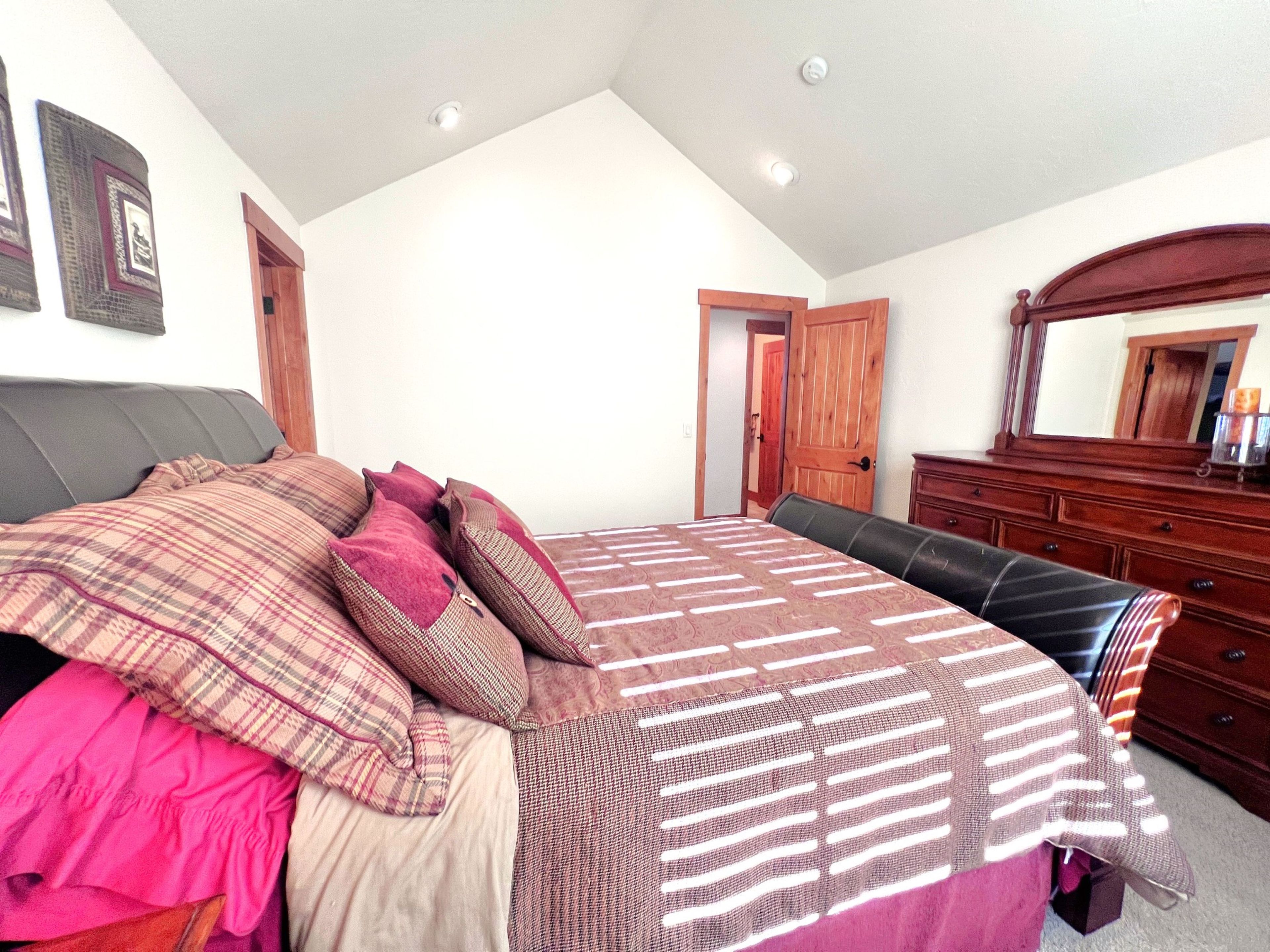 A bedroom with a bed, a dresser, a mirror, and a door.