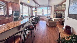 A spacious kitchen with a long island, bar stools, and a stone fireplace. - Eagles Nest • Mtn Views • Dog-Friendly • Ev Charger • Ski/Hike (Silverthorne)