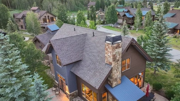 A large, multi-story house with a stone chimney, a patio with outdoor furniture, and a view of a forested area. - Eagles Nest • Mtn Views • Dog-Friendly • Ev Charger • Ski/Hike (Silverthorne)