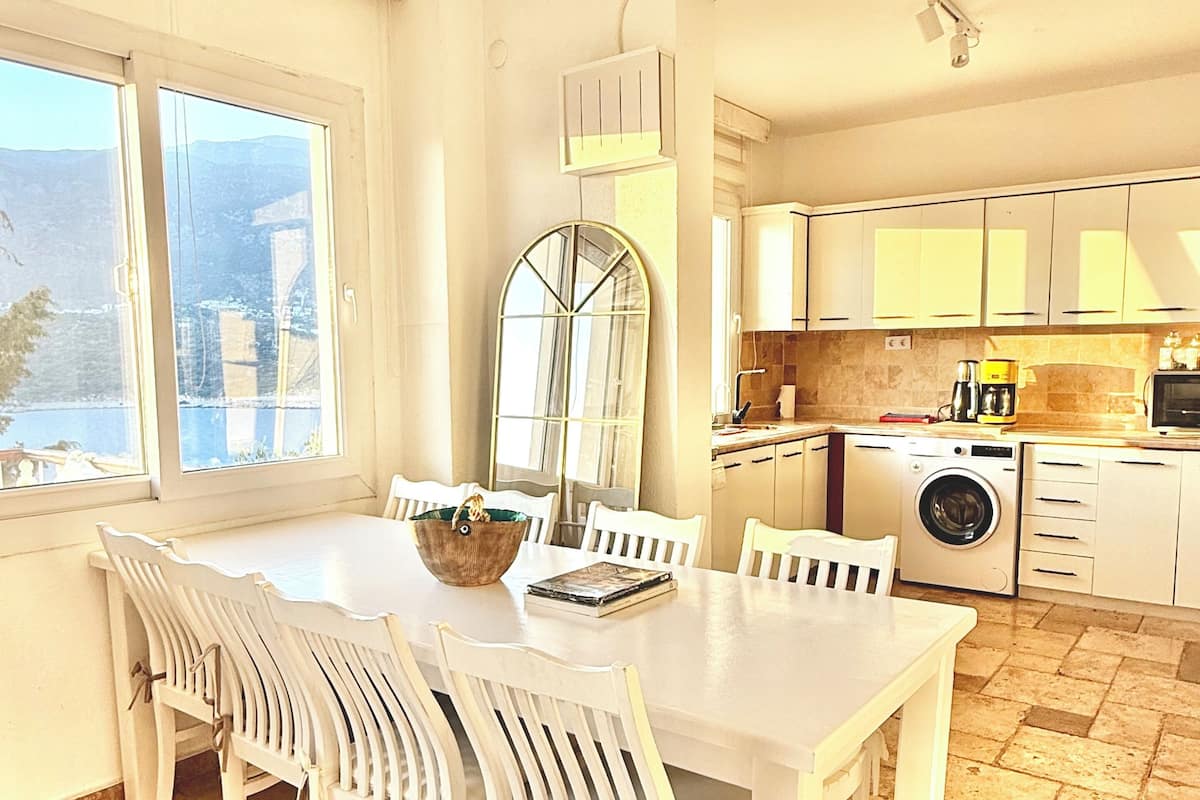 A spacious kitchen with a dining area, large windows, and a washing machine.