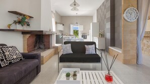 A modern living room with a fireplace, a sofa, a coffee table with plants, and a kitchen in the background. - 4204 Villetta Delle More by Barbarhouse (Melendugno)