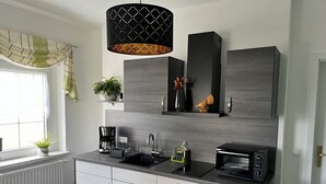A modern kitchen with a black countertop, stainless steel appliances, and a hanging pendant light.