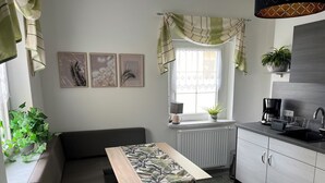 A compact kitchen with a dining area, a radiator, a coffee maker, and a potted plant.