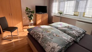A bedroom with a bed, a chair, a TV, a wardrobe, and a window with curtains.