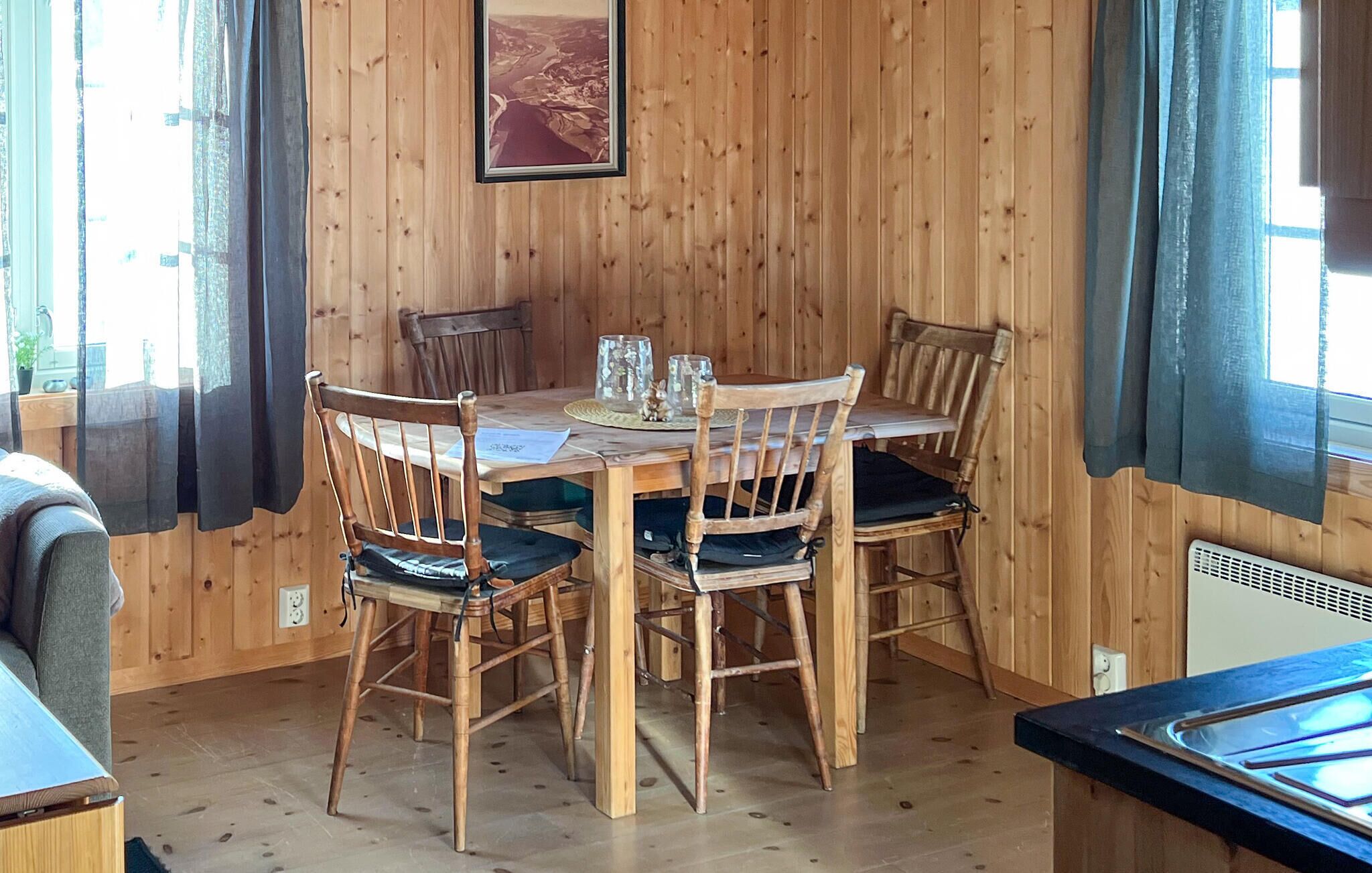 A wooden-paneled room with a dining table, four chairs, and a framed picture on the wall.