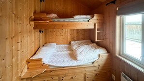 Habitación compacta tipo cabaña de madera con literas, una ventana pequeña y un calentador integrado.