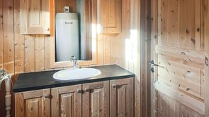 Un baño de madera con un lavamanos blanco, un espejo y un calentador de agua.