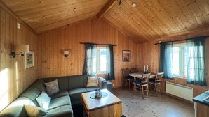 Acogedor interior de cabaña de madera con sofá, mesa de comedor y sillas.