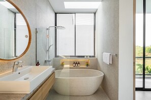 Een moderne badkamer met een vrijstaand bad, een grote spiegel en een raam met zonwering.