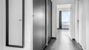 A modern hallway with white walls and dark flooring, leading to a room with a view of the sea.