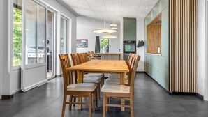 A modern kitchen with a large dining table, wooden chairs, pendant lights, and a view of the outdoors.