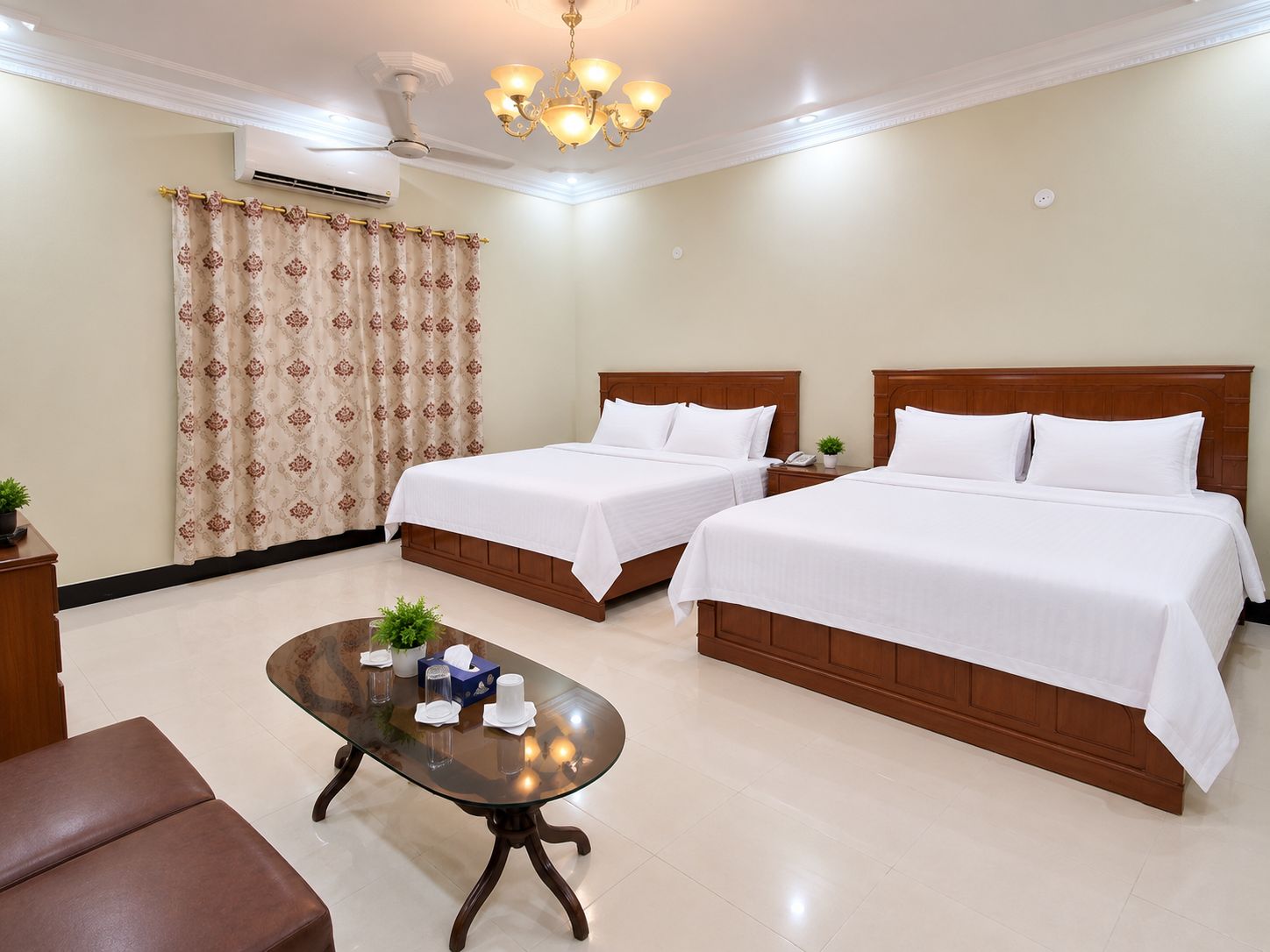 A hotel room with two beds, a glass coffee table, a ceiling fan, and a chandelier.