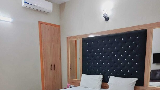 A bedroom with a bed, wooden wardrobe, and a wall-mounted air conditioner. - BNB Rose Lodge Family Guest House (Karachi)