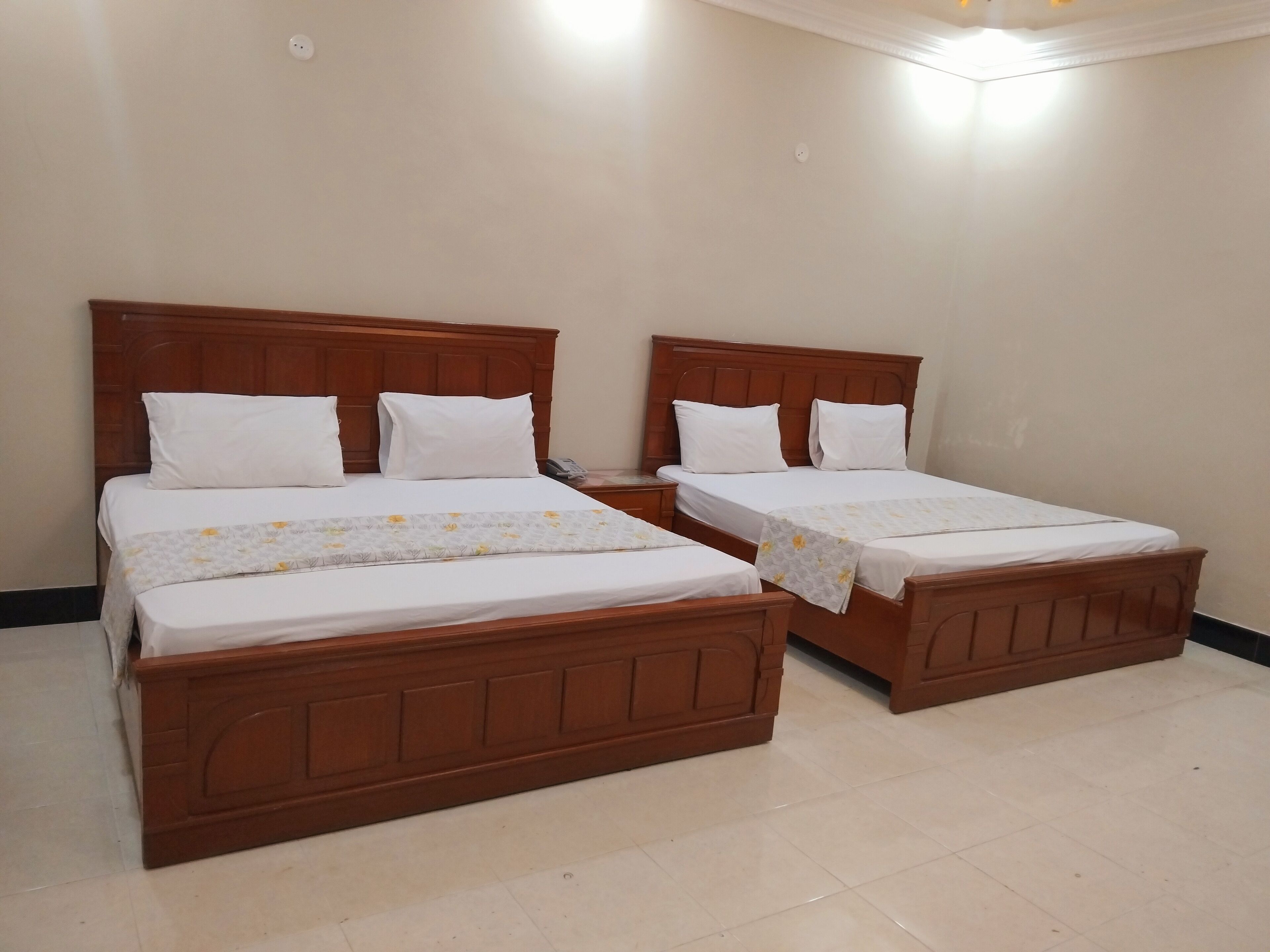 Two wooden beds with white bedding and floral-patterned blankets, a wooden headboard, and a tiled floor.