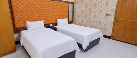 A hotel room with two beds, a wooden headboard, a nightstand, a wall-mounted light, and a door.