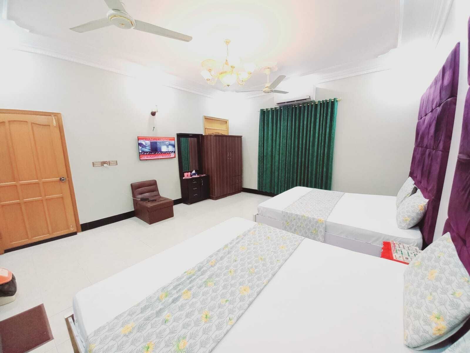 A hotel room with two beds, a TV, a wardrobe, a chair, and a ceiling fan.