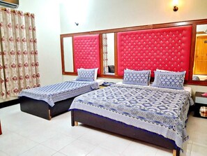 A hotel room with two beds, each with a patterned bedspread and pillows, a red upholstered headboard, and a mirror above the beds. - BNB Rose Lodge Family Guest House (Karachi)