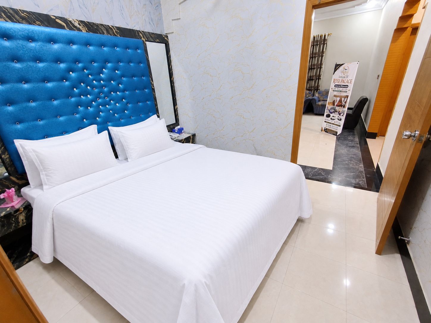 Habitación de hotel con una cama grande, cabecera capitonada, mesita de noche y puerta de madera.