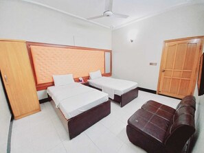 A hotel room with two single beds, a sofa, a wardrobe, and a ceiling fan. - BNB Rose Lodge Family Guest House (Karachi)