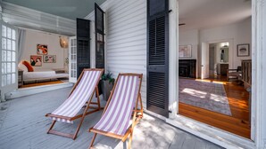 A spacious room with a wooden floor, a white wall, and a large window. There are two striped beach chairs and a potted plant. - Luxurious 4 Bedroom, 4.5 Bath Home (Charleston)
