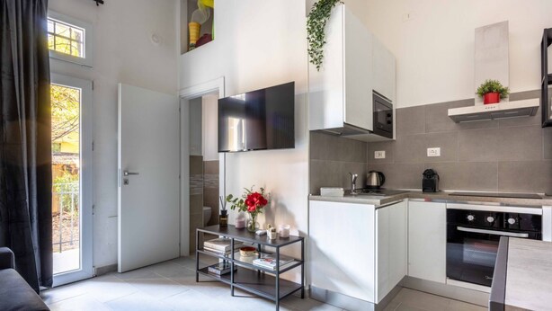 Una cocina compacta con armarios blancos, horno empotrado y televisor sobre la encimera.
