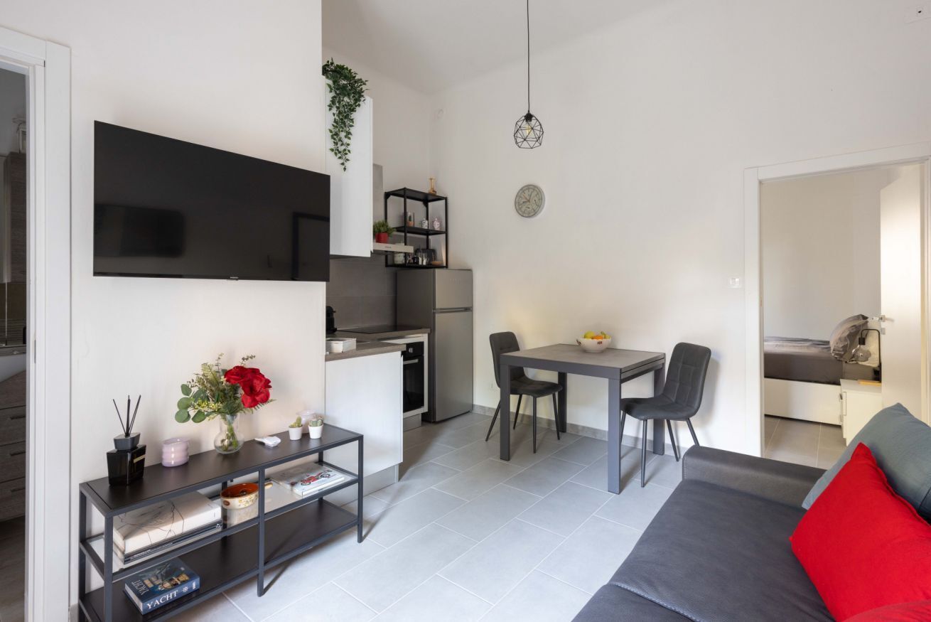 En kompakt opholdsstue med tekøkken, spiseplads og en sofa med røde puder.