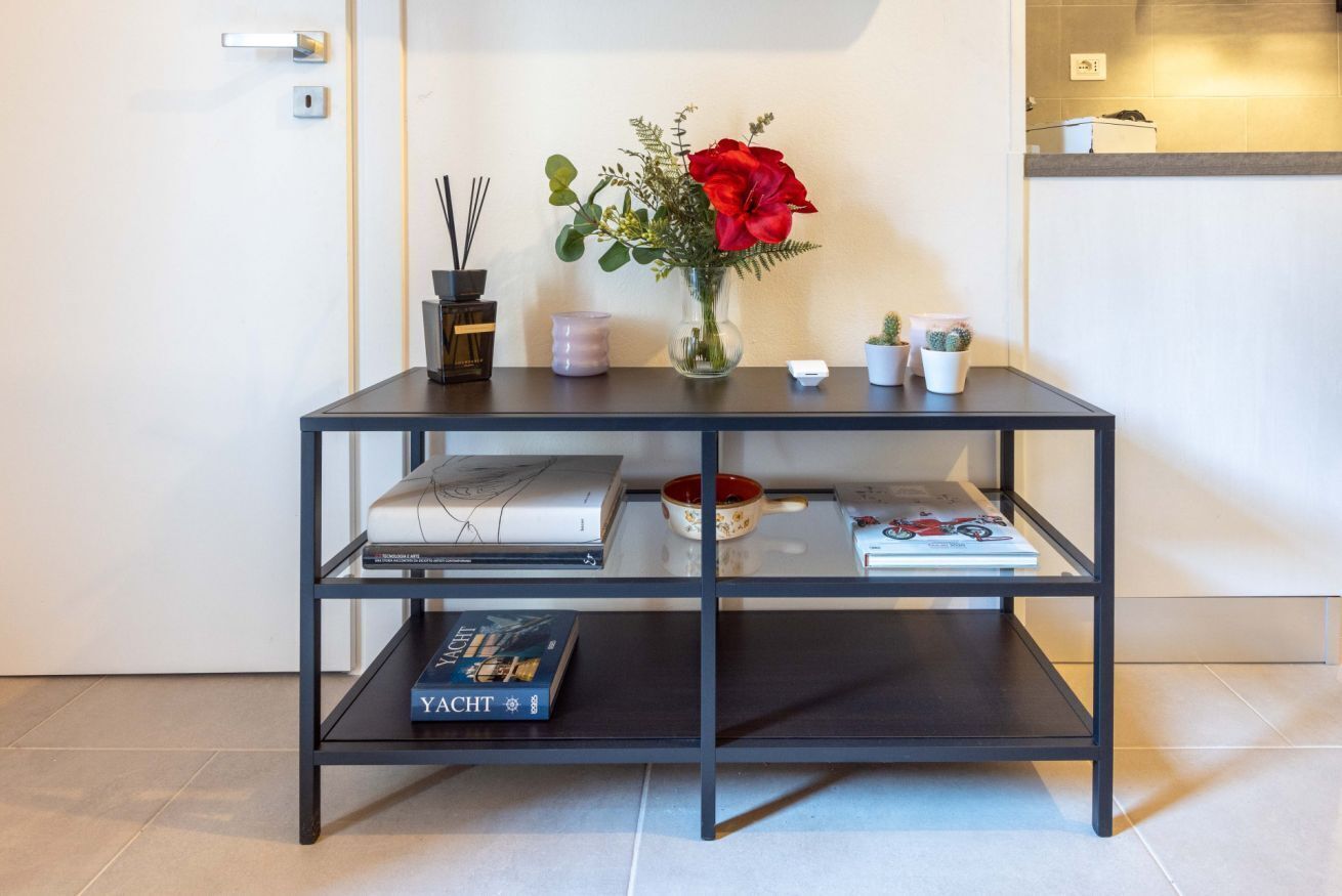 A modern, minimalist room with a black metal console table holding books, a vase with a red flower, and small decorative items.