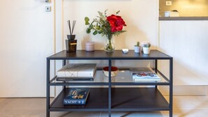 Una habitación moderna y minimalista con una consola de metal negro que sostiene libros, un florero con una flor roja y pequeños objetos decorativos.