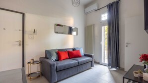 Una sala de estar moderna con un sofá gris, una mesita auxiliar pequeña, una mesa de centro negra y un espejo en la pared.