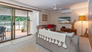 A living room with a sofa, a television, a guitar, and a lamp.