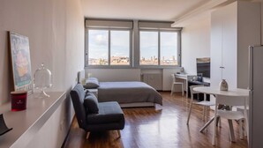 A modern bedroom with a large window, a bed, a desk, and a dining area.