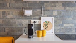 A kitchen with a stone backsplash, a coffee maker, two yellow mugs, and a framed artwork.