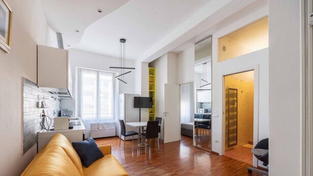 A modern living space with a wooden floor, a yellow sofa, a dining area, and a kitchen with white cabinets.