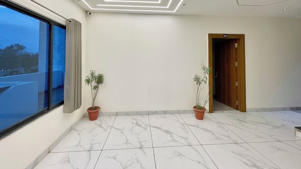 Una habitación amplia con un gran ventanal, una puerta de madera y dos plantas en macetas.