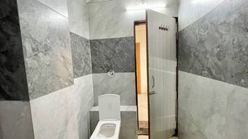 Un baño con inodoro, ducha y puerta que da a otra habitación.
