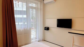 A hotel room with a bed, a TV mounted on the wall, a chair, and an air conditioning unit.