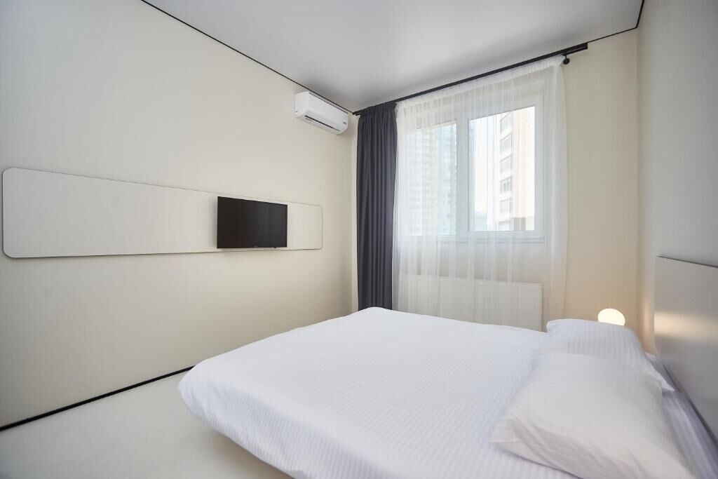 Une chambre d’hôtel moderne, équipée d’un lit, d’un téléviseur fixé au mur et d’une fenêtre avec des rideaux légers.