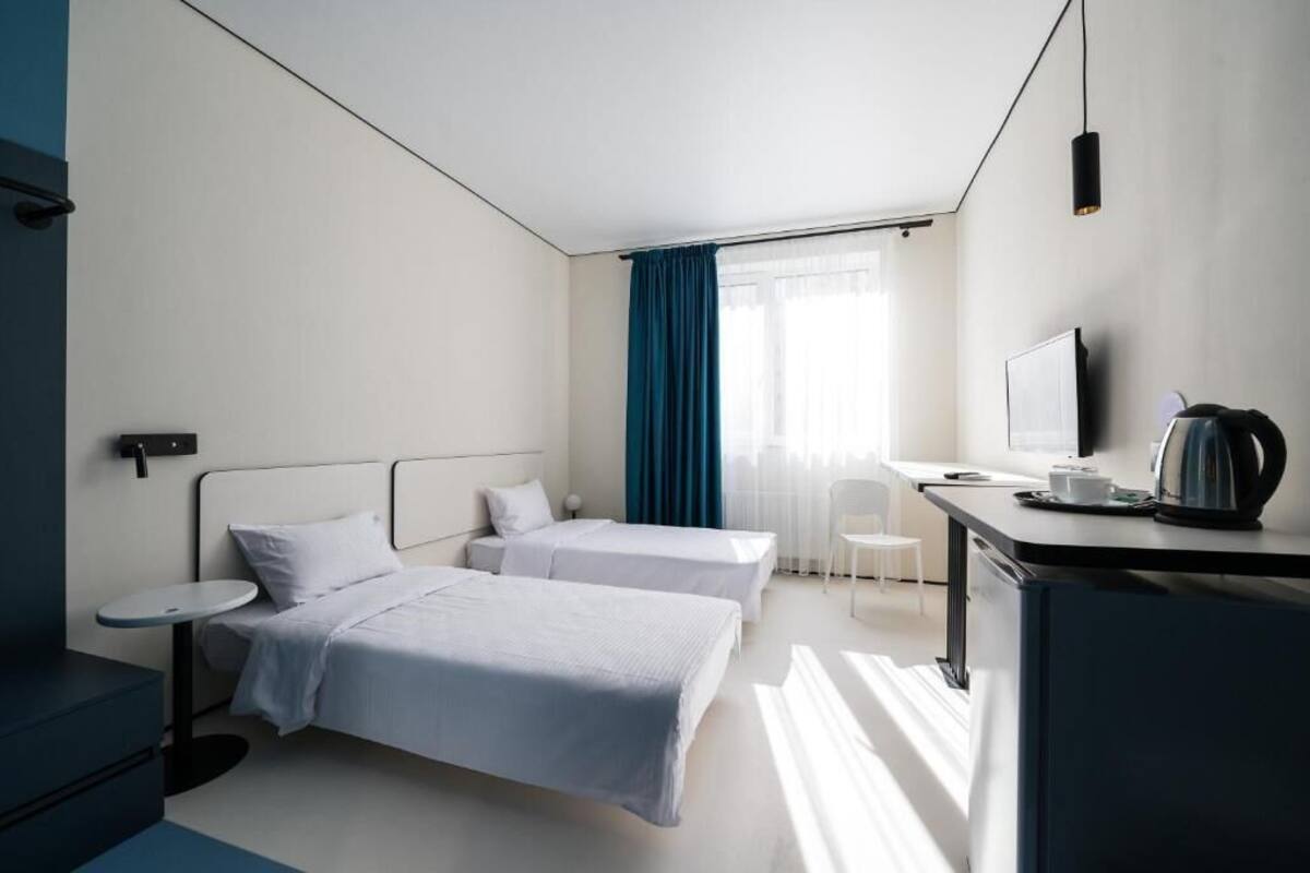 Una camera d'albergo moderna con due letti singoli, una scrivania con televisore, un bollitore e una sedia.