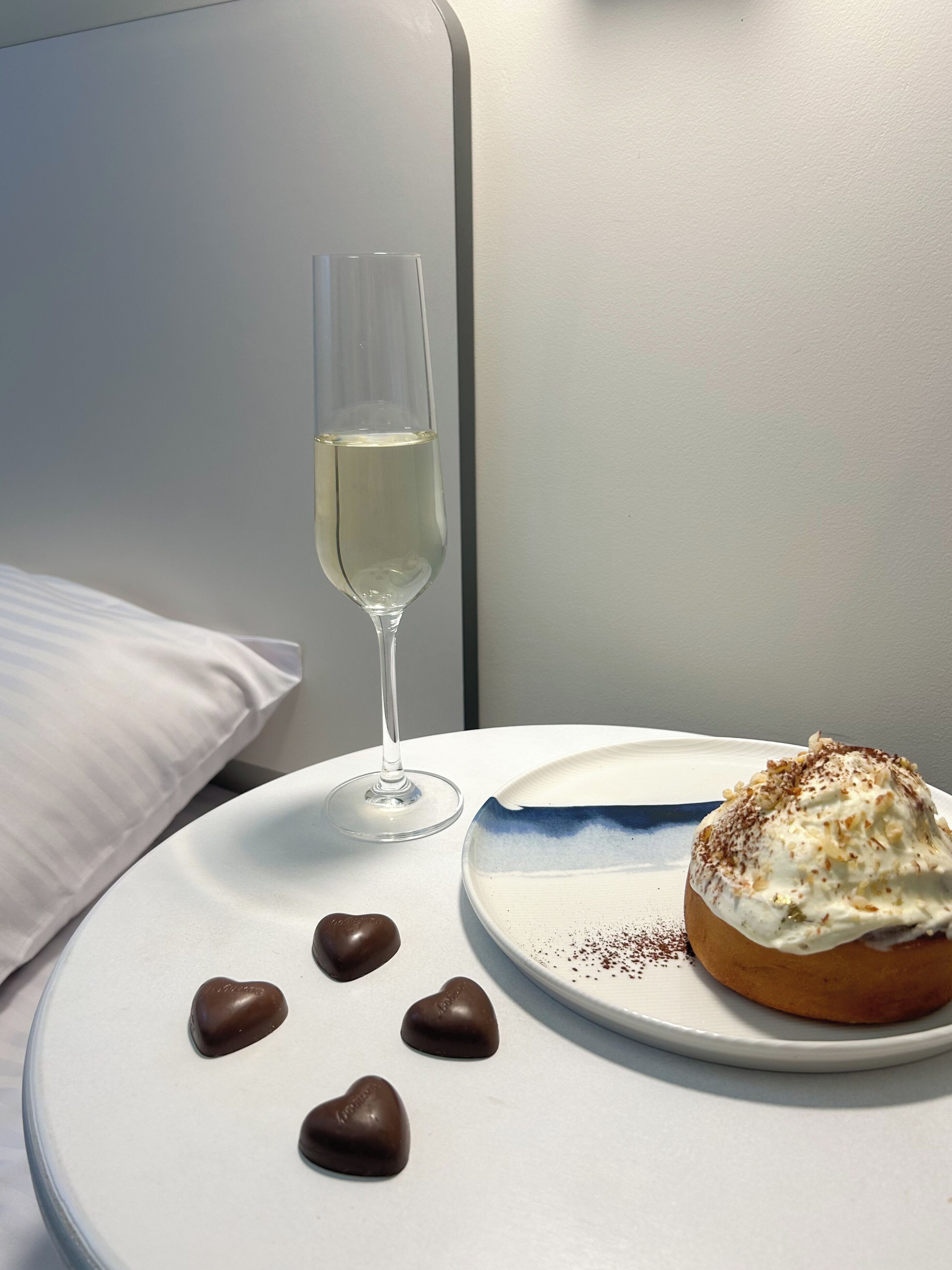 A neatly arranged breakfast setting with a plate of food, a glass of white beverage, and chocolate hearts on a white table.