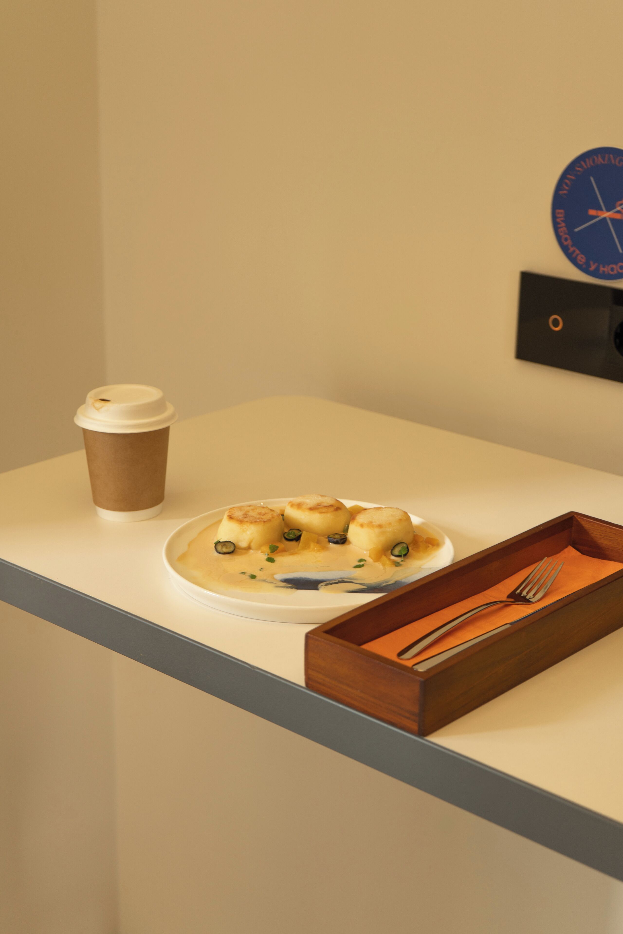 A table with a plate of food, a cup, and a wooden tray with a fork.