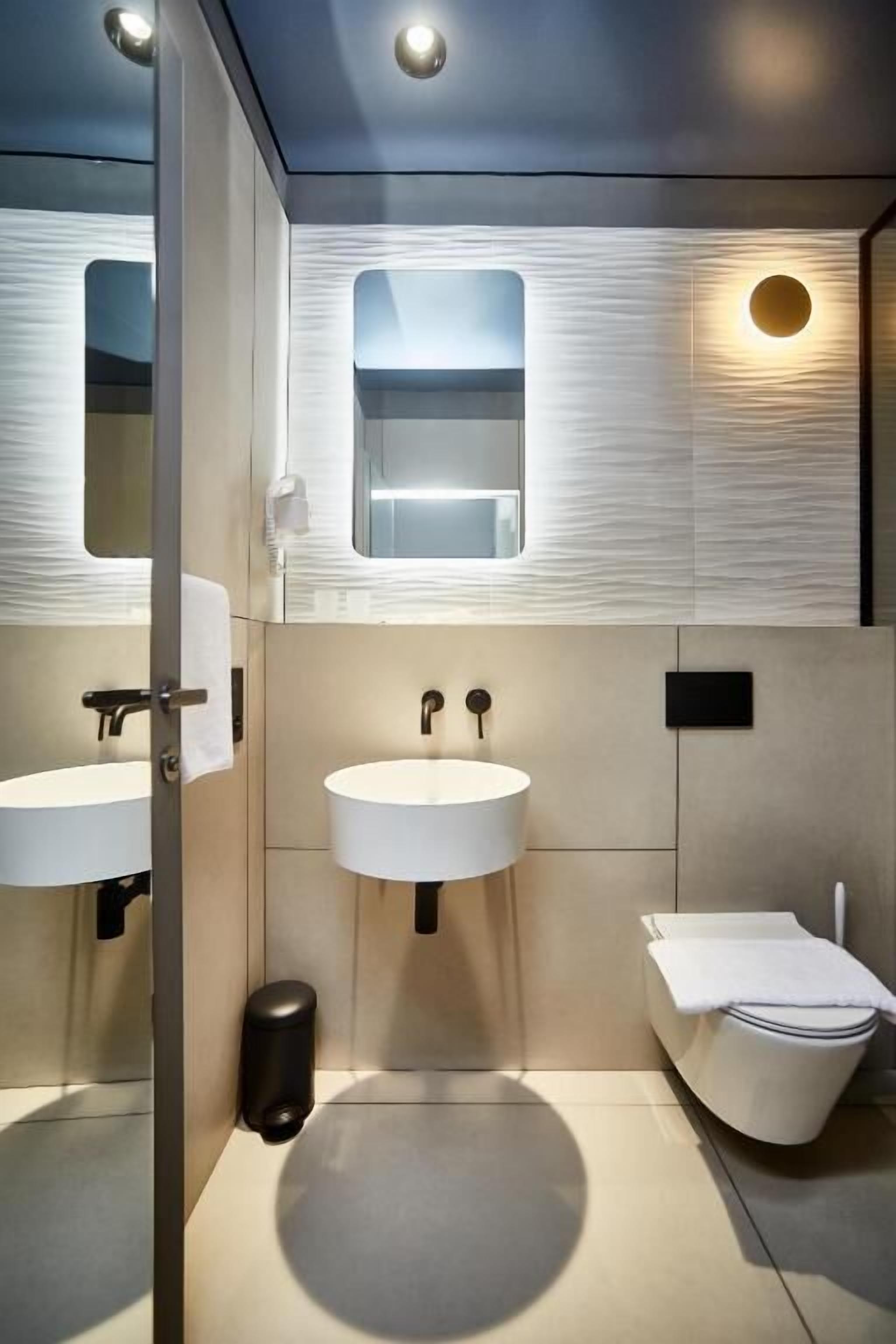 A modern bathroom with two sinks, a toilet, and a mirror.