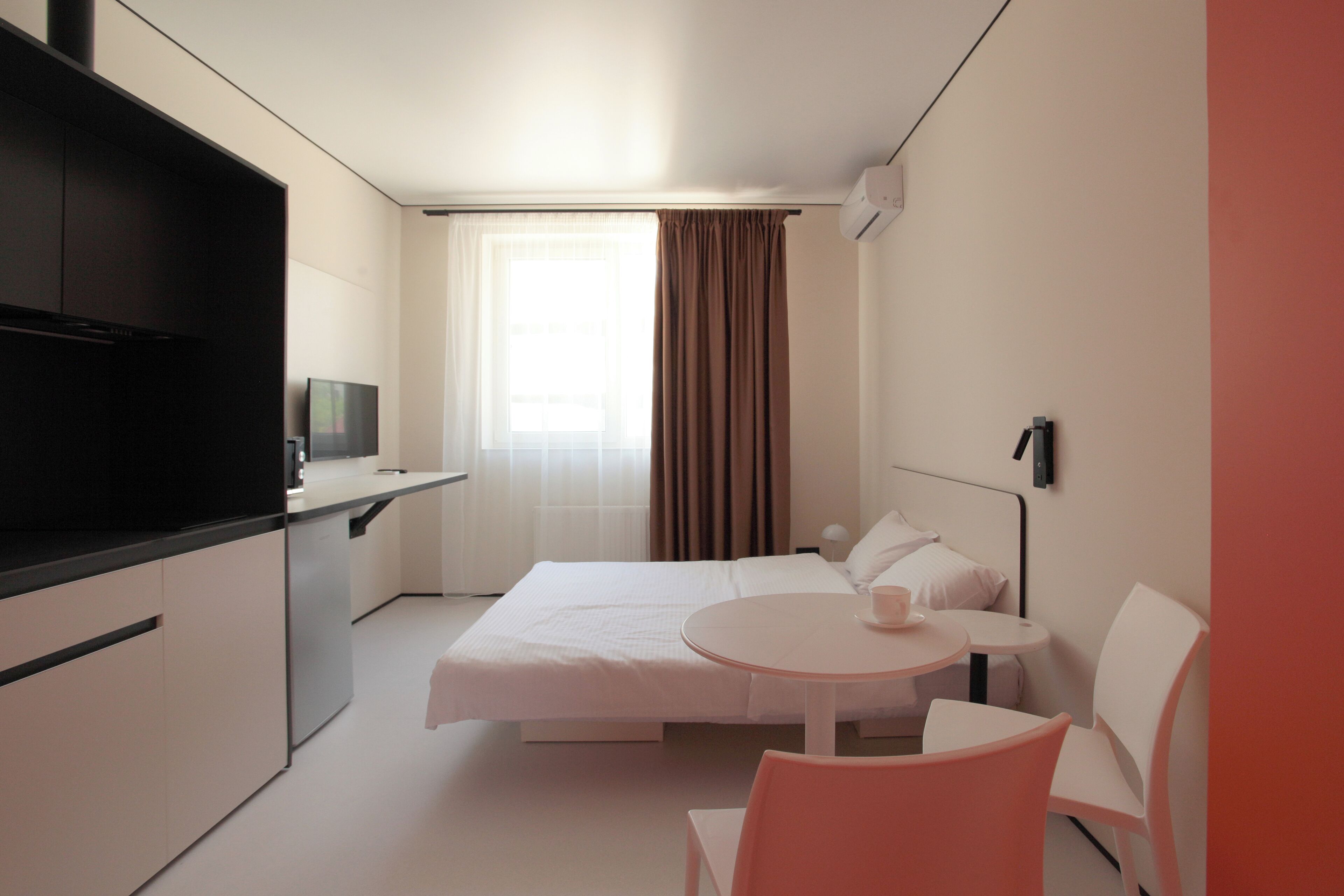 Habitación de hotel con cama, una mesita redonda con una taza, televisión y ventana con cortinas.