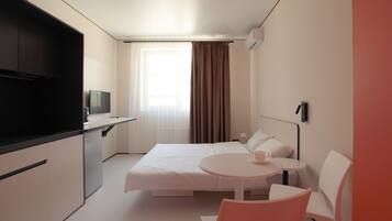 Habitación de hotel con cama, una mesita redonda con una taza, televisión y ventana con cortinas.