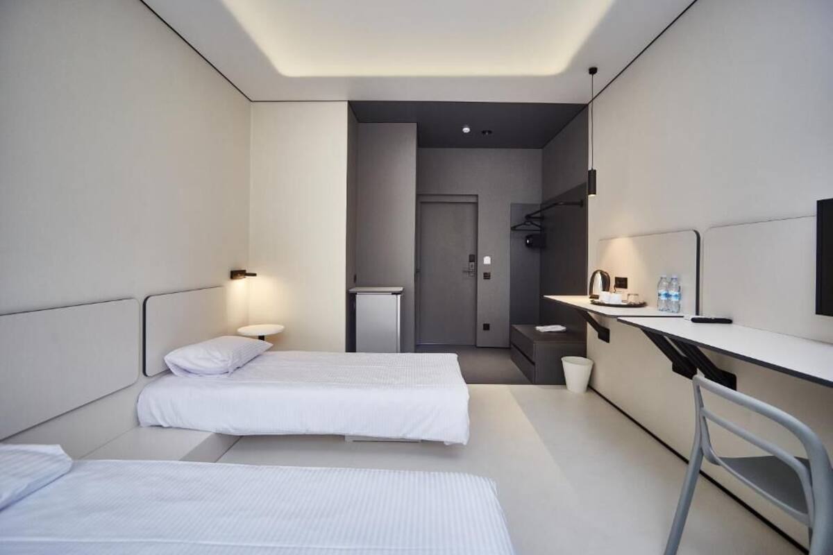 Camera d'albergo moderna con due letti singoli, una scrivania con sedia, un angolo cottura e un bagno.