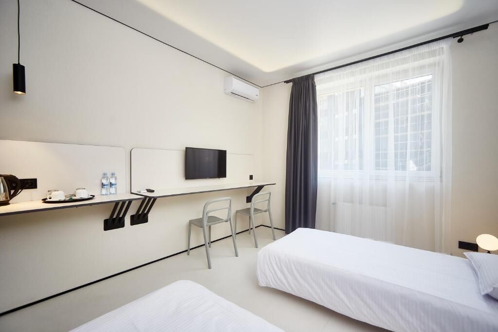 A hotel room with two beds, a desk with a chair, a TV, and a window with curtains.