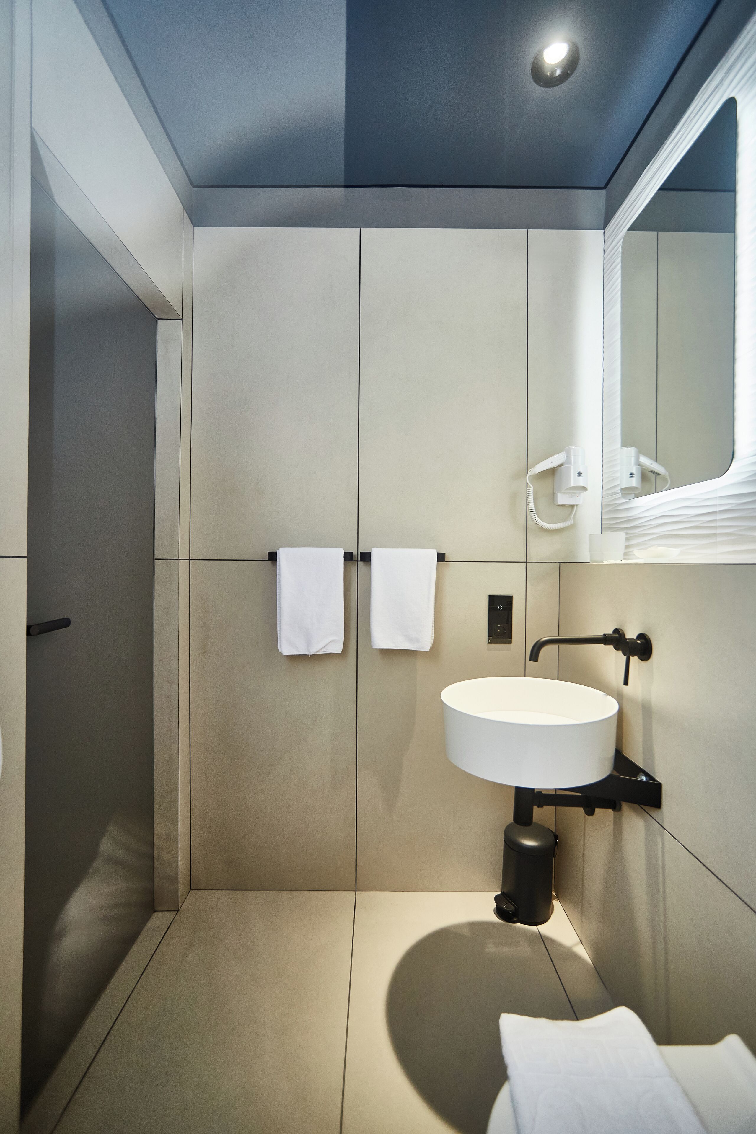 Une salle de bain moderne avec un grand lavabo, deux serviettes sur un porte-serviettes, un miroir et un espace douche.