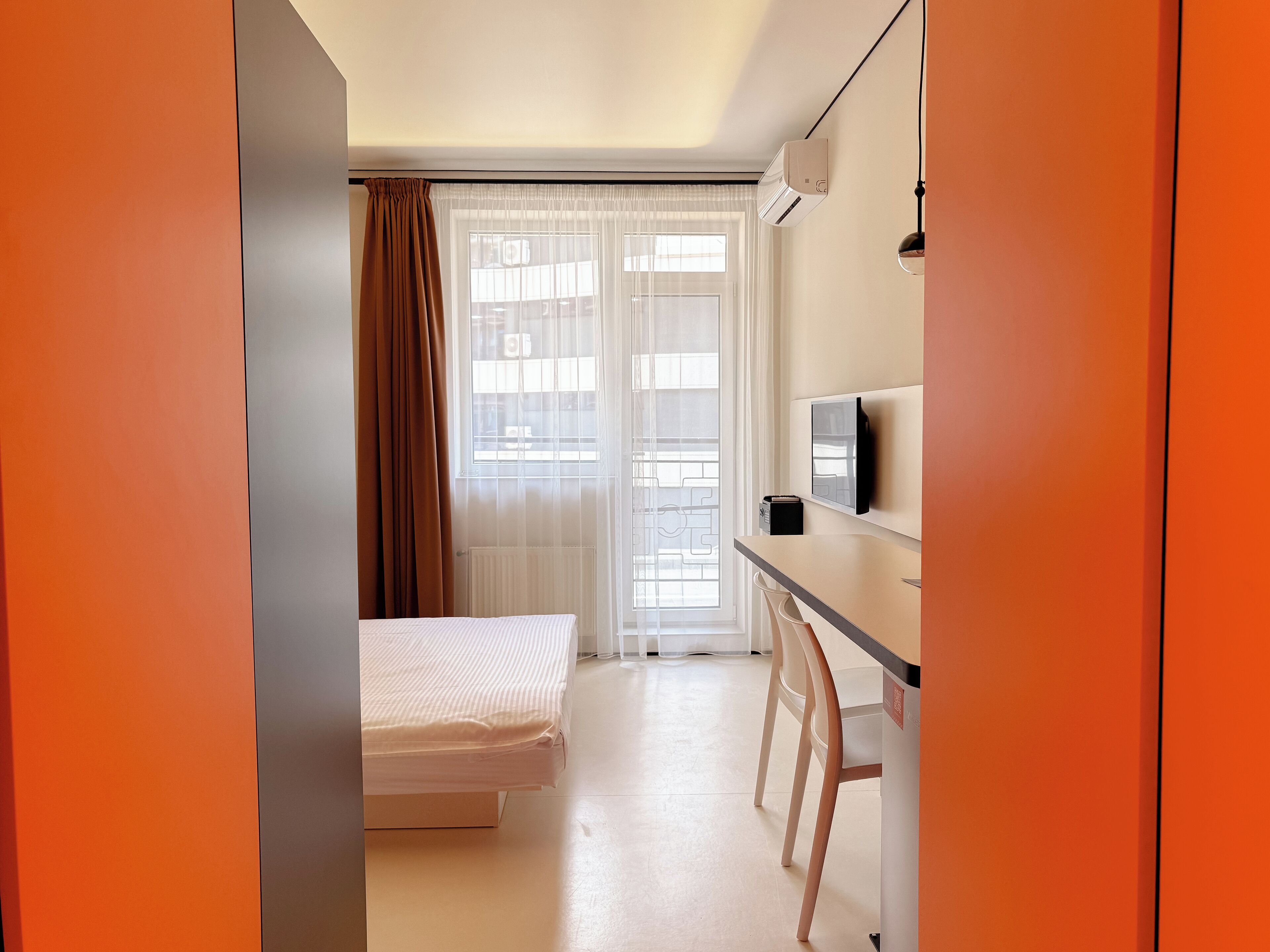 A small, bright room with a bed, a desk, and a TV.