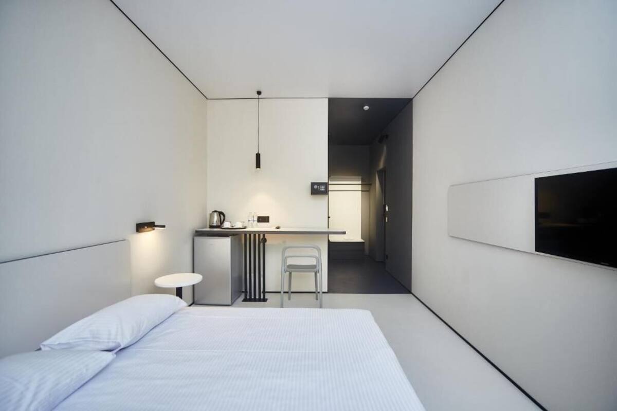 Una moderna camera d'albergo con un letto, una piccola scrivania, una sedia e un televisore a parete.