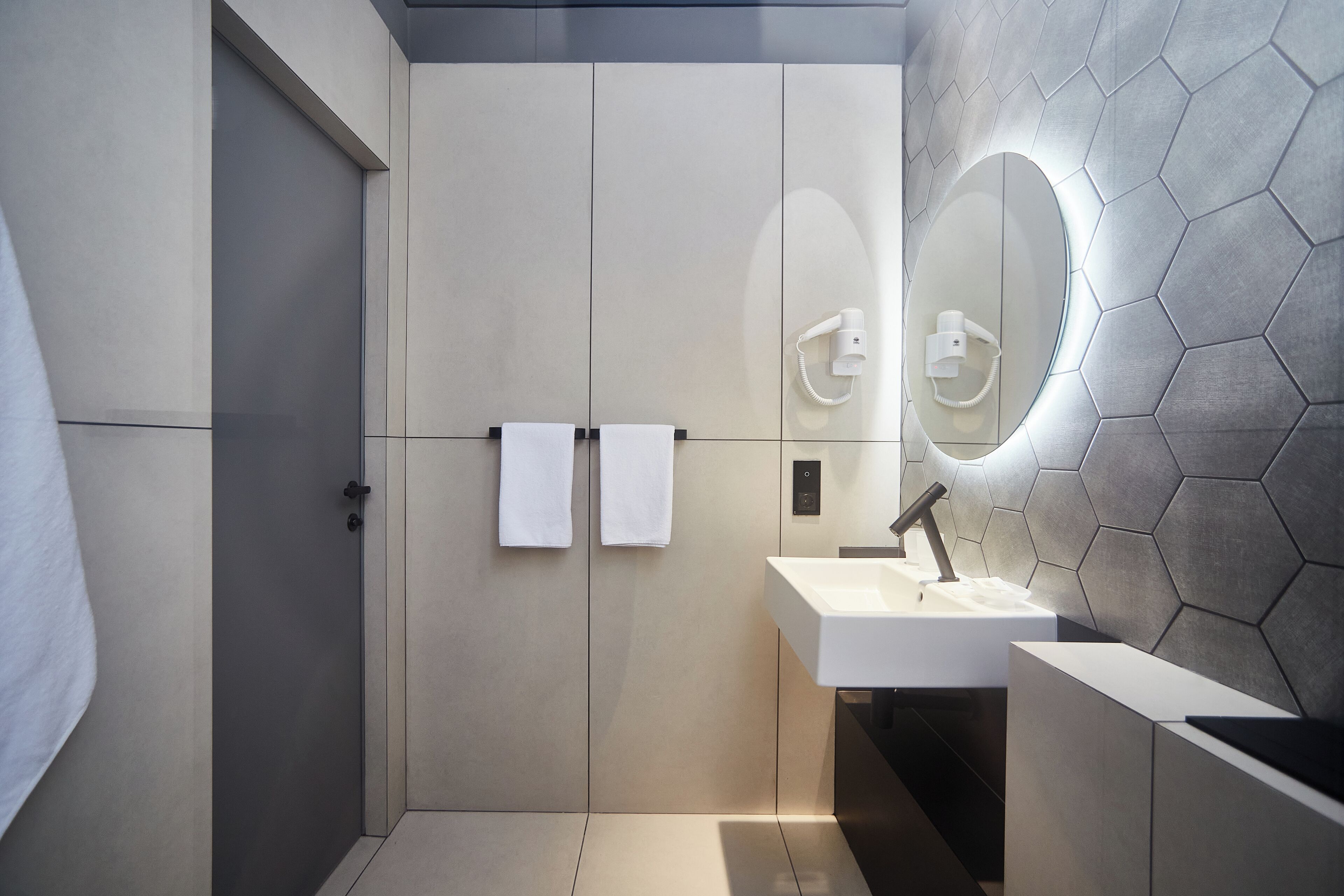 Un baño moderno con ducha a nivel, lavamanos con espejo y un perchero para toallas.