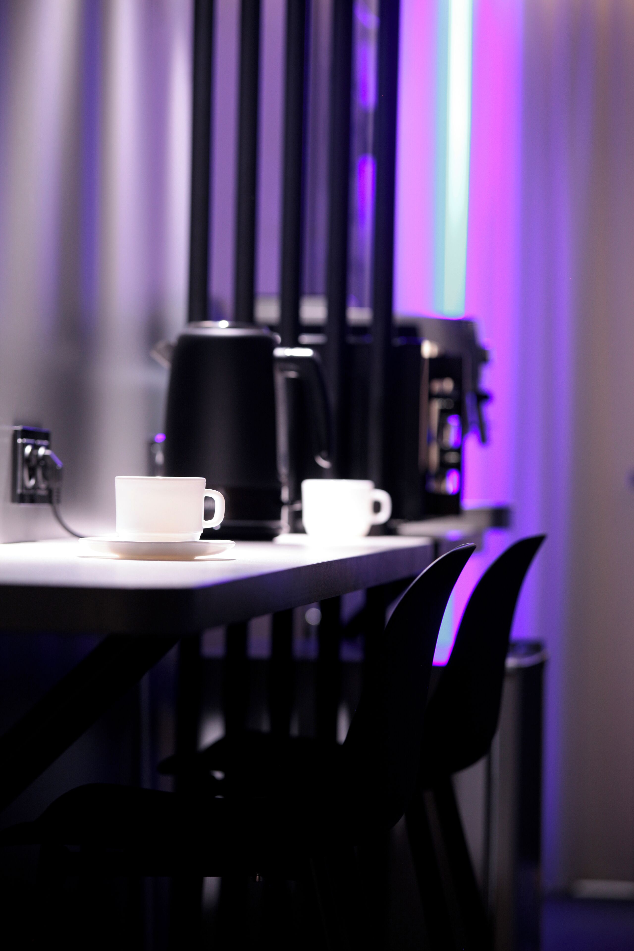 A table with a white cup and a black coffee maker.